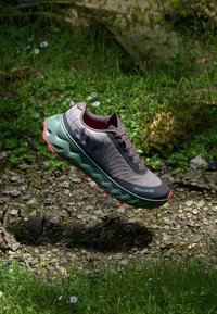 Chaussure de course légère avec une tige grise texturée, une semelle intermédiaire verte et une semelle extérieure rouge. Conçue pour l'adhérence sur différents types de terrain.