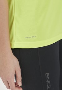 Lys gul, snabbtorkande träningsskjorta med strukturerad tyg, kombinerad med svarta leggings med en subtil logotyp i grått.