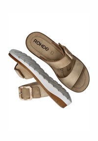 Beige sandaal met twee brede banden, een gesp-accent, en een witte zool met een textuur voor grip. De binnenvoering is zacht met een subtiel patroon.