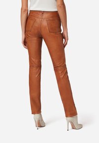 Braune Lederhosen mit taillierter Passform, sichtbaren Gesäßtaschen und Knienähten, kombiniert mit hellen High Heels.