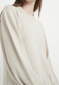 Pull beige clair à manches longues en tissu tricoté texturé, avec un col rond classique et une coupe décontractée à épaules tombantes.