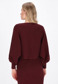 Bordeauxfarbener Strickpullover mit verkürztem Design, weiten Ärmeln und strukturiertem Stoff. Verfügt über gerippte Bündchen und ein kleines Logoschild auf der Rückseite.