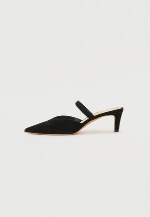 Μαύρη σουέτ γόβα slingback με μυτερή μύτη, χαμηλό τακούνι και λεπτή λουρίδα γύρω από τον αστράγαλο. Απαλή υφή και μινιμαλιστικός σχεδιασμός.