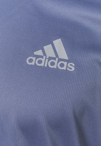 Tejido azul texturizado con el logo blanco de Adidas. El diseño es atlético con finas estrías visibles a lo largo del material.