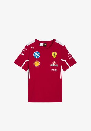 Czerwona koszulka z krótkim rękawem z białymi detalami, z logo Ferrari i wieloma logo sponsorów, wykonana z lekkiego materiału.