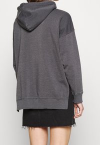 Sweat-shirt gris à capuche avec une coupe décontractée, présentant un ourlet et des poignets côtelés, assorti à une jupe en jean noire.