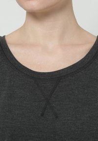 Top gris oscuro con un escote redondeado, que presenta un detalle de punto de cruz en el cuello. El material parece suave con un acabado ligeramente texturizado.