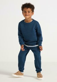 Dunkelblaues Sweatshirt und passende Sweatpants, aus weichem Stoff, mit gerippten Bündchen und einem geschichteten weißen Hemd darunter.