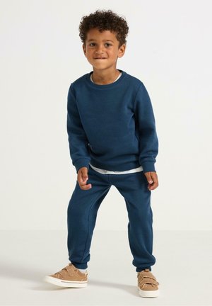 Dunkelblaues Sweatshirt und passende Sweatpants, aus weichem Stoff, mit gerippten Bündchen und einem geschichteten weißen Hemd darunter.