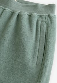Fleece joggers i en dæmpet grøn farve med ribbet talje, sidelomme og blød, struktureret stofoverflade.