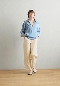 Camicia di jeans over-size azzurra chiara con scollatura a V profonda, abbinata a pantaloni larghi color crema. Le scarpe beige slip-on completano l'outfit.