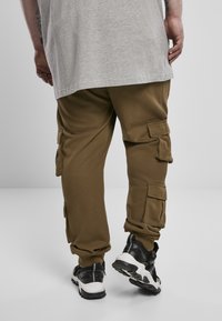 Kaki cargo bukser med flere sidelommer, elastiske manchetter og et blødt, struktureret stof. Sammen med sorte og hvide sportsko.