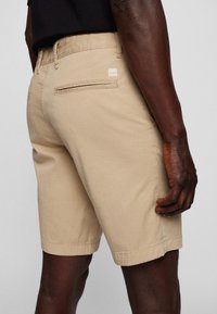 Ljusbeiga bomullsshorts med smal passform, med en bakficka med dragkedjestängning och en liten märkning på midjebandet.