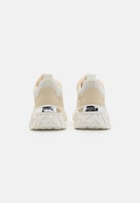 Beige og hvite sneakers med en kraftig såle. Har en teksturert hæl, refleksdetaljer og logodetaljer bak.