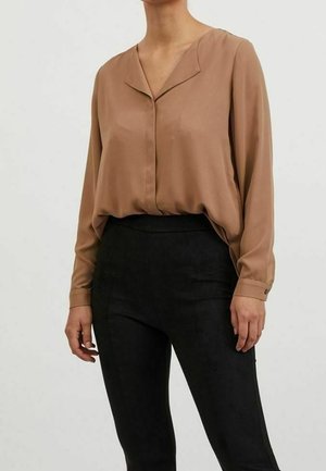 Blusa marrone a maniche lunghe con scollatura a V e un taglio leggermente rilassato, abbinata a pantaloni neri a vita alta realizzati in un materiale testurizzato.