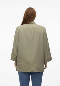 Blazer oversize vert olive avec un col cranté et des manches larges, fabriqué à partir d'un tissu lisse, présentant un design épuré et minimaliste.