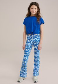 Zila īsā krekla ar sasietu detaļu, pāris ar flared biksēm zilo un baltā viļņu rakstā. Modelis valkā baltas kedas.