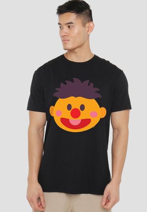 Schwarzes Baumwoll-T-Shirt mit einem großen, bunten Cartoon-Gesicht, das einen runden gelben Kopf, lila Haare, eine rote Nase und einen lächelnden Gesichtsausdruck zeigt.