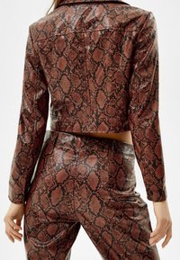 Veste courte et pantalon en simili cuir marron avec un motif python noir ; présente des épaules structurées et une texture lisse et brillante.