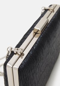 Pochette noire texturée avec un fermoir métallique et une chaîne. Elle présente une forme rectangulaire élégante et une surface striée pour une apparence distincte.