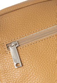 Tessuto in pelle color tan con una superficie texturizzata; presenta una zip argentata e una cucitura lungo il bordo. La zip è parzialmente aperta.