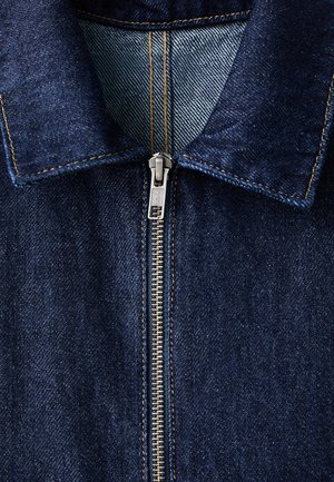 Teksas jakna tamnoplave boje, sa srebrnim patentnim zatvaračem, špicastim ovratnikom i vidljivim detaljima šavova duž spojnih linija.