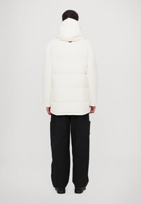 Veste blanche matelassée à capuche, avec des sections matelassées. Associée à un pantalon cargo noir ample. Design minimaliste avec une texture lisse.