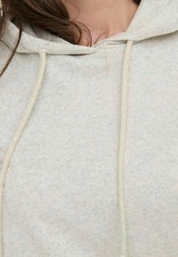Nahaufnahme eines hellgrauen Hoodies mit Kordelzügen und etwas dunklem Haar, das auf die Schulter ruht.
