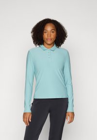 Long-sleeve polo shirt in light blue, made from a smooth, stretch fabric. Features a collar and four front buttons. Paired with dark pants.