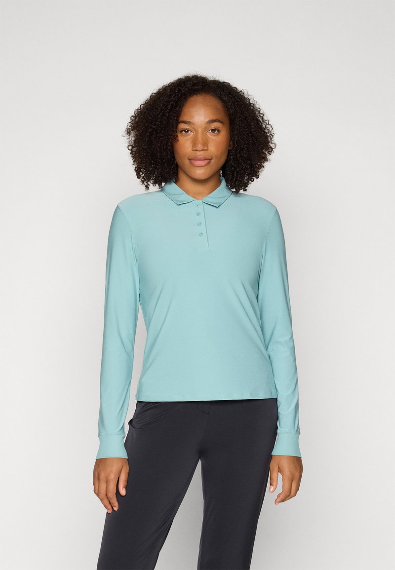 Long-sleeve polo shirt in light blue, made from a smooth, stretch fabric. Features a collar and four front buttons. Paired with dark pants.