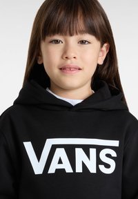 Zwarte hoodie met een groot wit 'VANS' logo. Het materiaal lijkt zacht en gestructureerd, met een ruime kap en een klassieke snit.