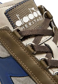 Sneaker in pelle beige e tessuto marrone, con un accento blu, lacci marroni, occhielli in metallo e un'etichetta tessuta testurizzata.