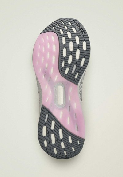 La semelle de la chaussure présente un design en caoutchouc gris avec une semelle intermédiaire rose et des motifs de grip texturés. Elle contient des accents blancs en forme de pods pour la traction.