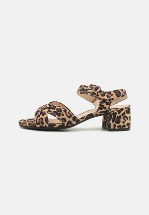 Løveprint sandal med kryssende stropper, rund tå og lav blokkhels. Laget av mykt materiale med en teksturert finish.