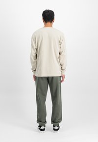 Svetlé béžová košeľa s dlhým rukávom a zelené teplákové nohavice s voľným strihom, mäkkou textúrou a stočenými lemami, doplnené čiernymi teniskami.