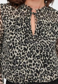 Blouse à imprimé léopard avec un col fendu et un col à volants. Tissu léger et transparent présentant des taches noires et fauves. Manches longues.