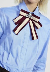 Camicia azzurro chiaro con colletto e papillon a righe bordeaux e crema, caratterizzato da un gruppo di gemme trasparenti come dettaglio.