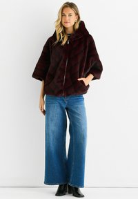 Burgundy faux fur jacket with a hood, featuring a diagonal quilted pattern and front zipper. Paired with wide-leg blue denim jeans and black boots.