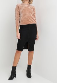Lichtbruin gestructureerd sweater met lange mouwen, gecombineerd met een nauwsluitende zwarte midi-rok met een split aan de voorkant en zwarte enkellaarsjes.