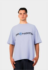 Licht lavendel oversized t-shirt met de tekst "PROHIBITED" in zwart en blauw, ronde halslijn, korte mouwen en een losse pasvorm.