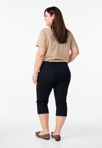 Pantaloni capri neri con un design aderente, due tasche posteriori, indossati con una maglietta beige e ballerine con stampa leopardata. Capelli che scendono oltre le spalle.