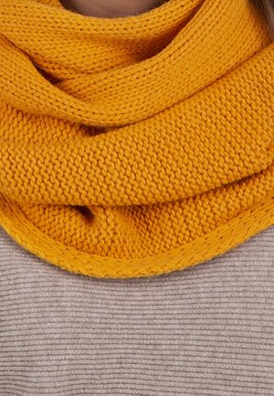 Écharpe jaune vif en tricot enroulée autour du cou sur un pull gris clair côtelé.