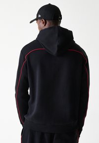 Sweatshirt preto com capuz, com detalhes em vermelho ao longo das costuras, mangas longas e um acabamento canelado. O material parece suave e texturizado.