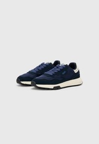 Navy blue sneakers with a mix of suede and mesh materials, featuring thick laces, a white sole, and curved accents on the heel.