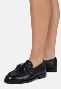 Mocassins pretos feitos de couro texturizado com padrão de crocodilo, apresentando um bico arredondado e um salto baixo em bloco.
