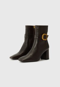 Brown leather ankle boots with a square toe, chunky heel, and a decorative gold buckle detail on the side. Zipper closure at the back.