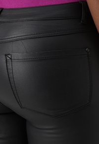 Black faux leather pants featuring a rear pocket with a subtle stitching detail and smooth texture. The waistband is visible above the pants.