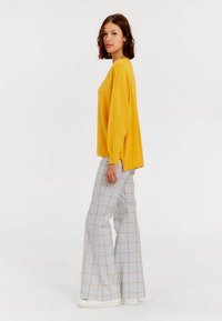 Pull oversized jaune avec des manches longues, associé à un pantalon large à carreaux dans des tons de bleu clair, beige et blanc. Tissu texturé et style décontracté.