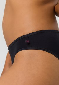 Schwarzer Bikini-Slip mit nahtlosem Design, hergestellt aus glattem Material. Enthält ein kleines Logotag an der Seite mit dezenten Nähdetails.