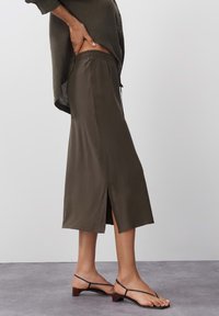 Oliivinvihreä, kevyt hame, jossa on joustava vyötärönauha, polvenpituinen, sivuhalkioilla ja sileä tekstuuri. Yhdistetty mustien sandaalien kanssa.